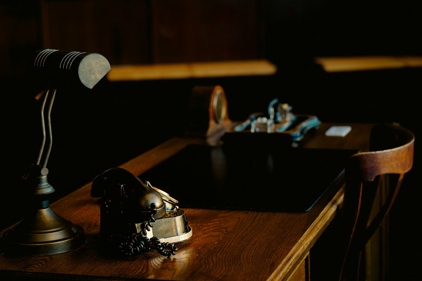 A vintage desk lamp and telephone receiver sit on a wooden desk.