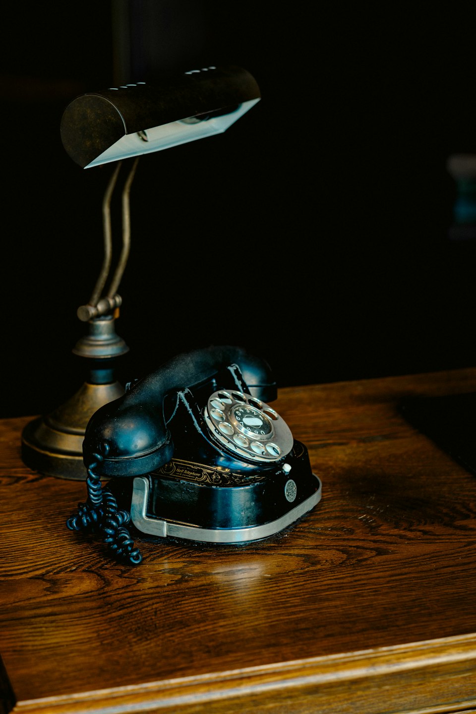 Vintage black rotary telephone sitting on a wooden desk.