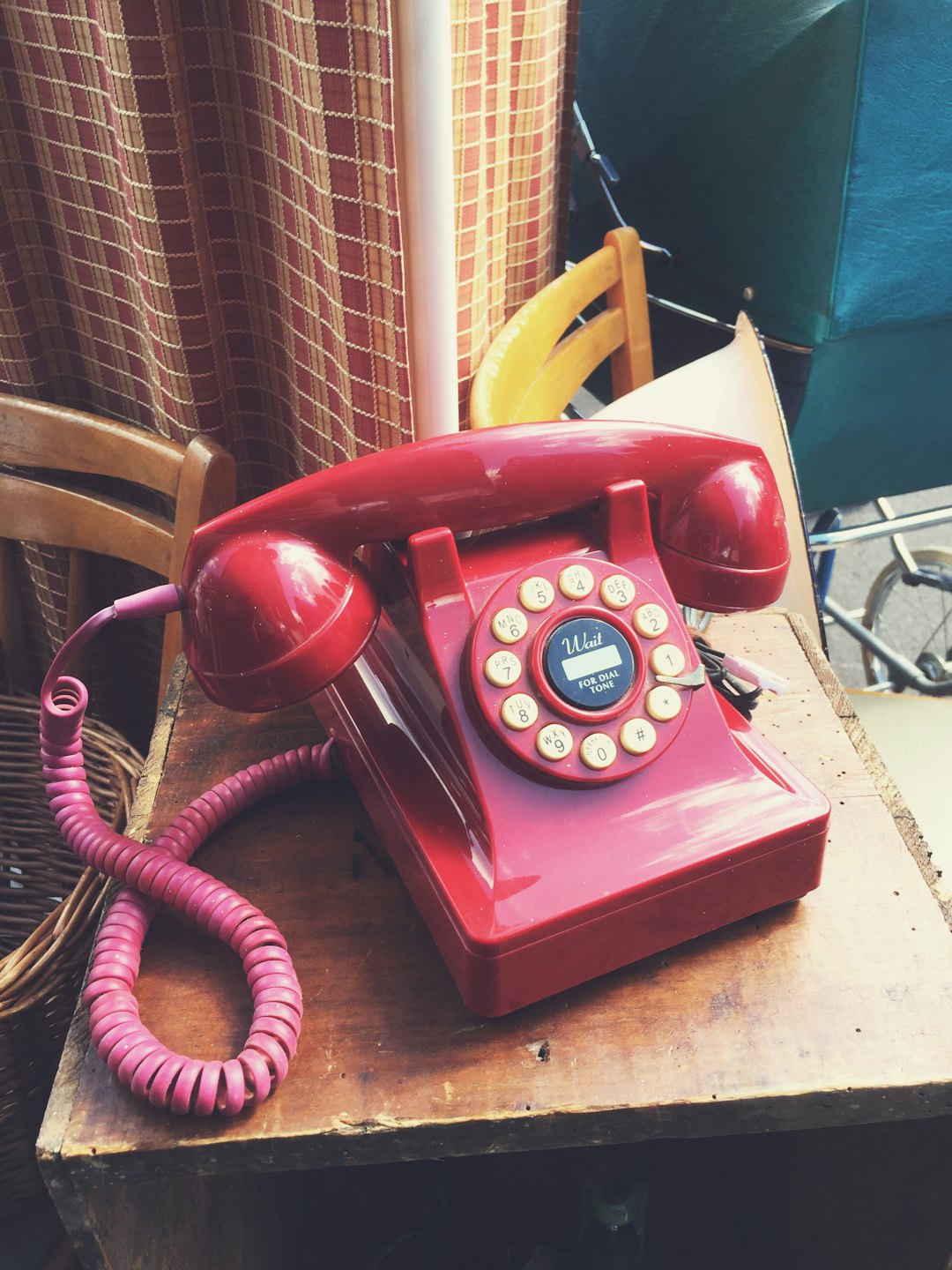 Red vintage rotary telephone sits on a rustic wooden table.